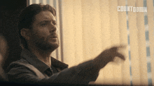 a man with a beard stands in front of a window with a sign that says countdown on it