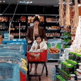 a woman pushes a little girl in a shopping cart in a grocery store