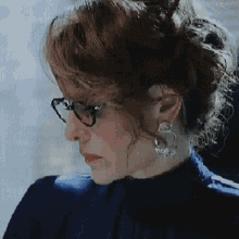 a woman wearing glasses and earrings is looking at the camera .