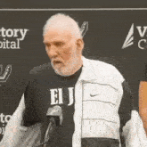 an older man with a beard is standing in front of a microphone .