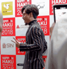 a man in a striped jacket is standing in front of a wall that says nippon haku