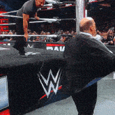 a man in a suit is standing in front of a wrestling ring with a raw banner behind him