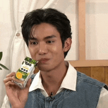 a young man in a denim vest is holding a box of tipco juice