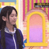 a woman in a blue jacket is standing in front of a brick wall with a yellow archway ..