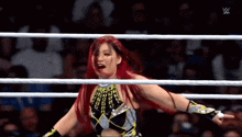 a woman with red hair is standing in a wrestling ring with a crowd watching .