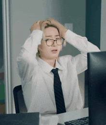 a man wearing glasses and a tie is sitting at a desk in front of a computer