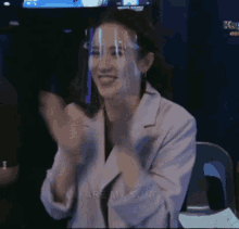 a woman wearing a face shield is clapping her hands in a room .