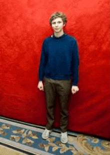 a young man is standing in front of a red wall .