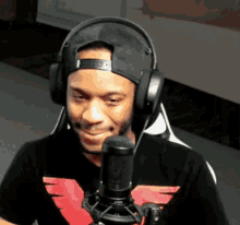 a man wearing headphones and a hat smiles in front of a microphone