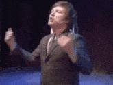 a man in a suit and tie is singing into a microphone while standing on a stage .