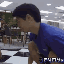 a man in a blue shirt is squatting on a checkered floor with the word fumys on the bottom