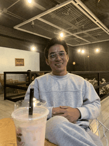a man wearing glasses sits next to a pink drink