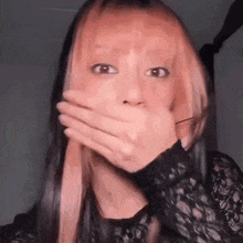 a woman with long pink hair is covering her mouth with her hands .