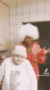 a woman in a white afro wig is standing next to an older woman in a pink jacket .