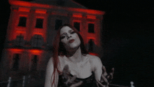 a woman with red hair is standing in front of a building that has red lights on it