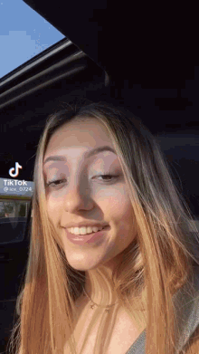 a young woman is smiling while sitting in a car with a tiktok logo on the bottom right