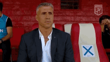 a man in a suit is sitting in a red and white striped chair with a blue x on the back .