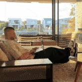 a man sits on a couch with his feet up and a laptop on his lap