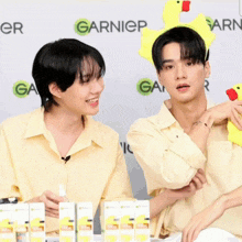 two young men are sitting in front of a garnier banner