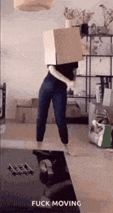 a woman is dancing with a cardboard box on her head in a living room .