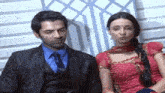 a man and a woman are sitting next to each other on a couch . the woman is wearing a red dress .