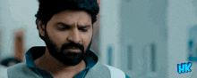 a man with a beard is looking down with hk written in blue letters