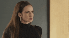 a woman wearing a black turtleneck and earrings is looking to the side