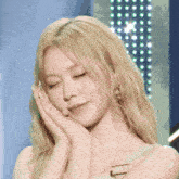 a blonde woman with her eyes closed and her hand on her face
