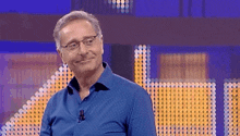 a man wearing glasses and a blue shirt is smiling in front of a blue background