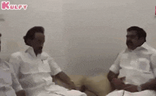 a group of men in white shirts are sitting on a couch talking to each other .