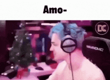 a man with blue hair is wearing headphones while sitting at a computer .