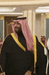 a man in a black robe with a yellow sash stands in a room