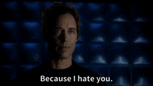 a man in a black shirt is standing in front of a blue wall and saying because i hate you .