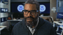 a man with glasses and a beard is standing in front of a computer monitor