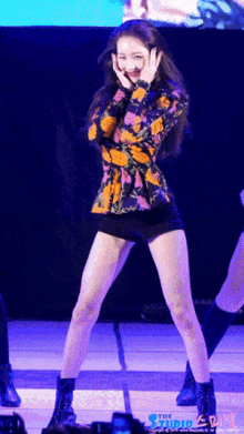 a woman in a floral top and black shorts is dancing on a stage