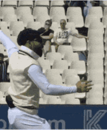 a man in a white vest is standing in front of a row of white seats .