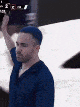 a man with blue hair and a beard is standing in front of a scoreboard with the number 2 on it .