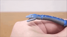 a person is holding a toy dinosaur in their hand and it looks like a snake .