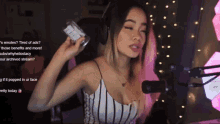 a woman wearing headphones and a striped tank top stands in front of a microphone holding a bottle