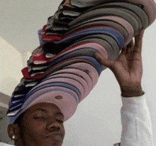 a man wearing a hat is holding a stack of hats above his head .