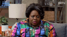 a woman is sitting on a couch wearing a colorful shirt and a lamp .
