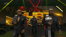 three men in suits and sunglasses are walking on a stage in front of a aew logo