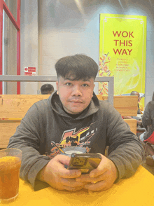 a man sits at a table with a phone in front of a sign that says wok this way