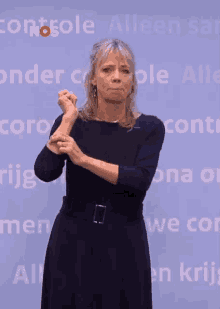 a woman in a black dress stands in front of a wall that says controle alleen san
