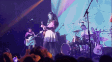 a woman playing a guitar and a man playing drums on a stage