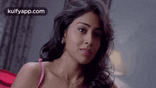 a woman in a pink bra is sitting on a bed looking at the camera .