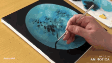 a person is painting a blue circle on a canvas with the words made in animatica on the bottom