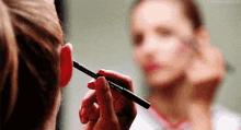 a woman is applying makeup to her face with a brush .