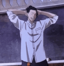 a man in a white shirt is standing in front of a blackboard with his hands behind his head .
