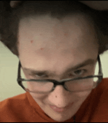 a close up of a person wearing glasses and an orange shirt